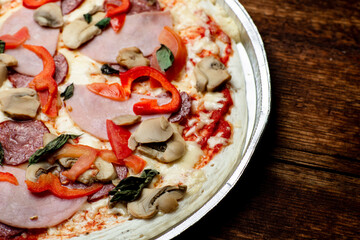 Pizza edge closeup on a wooden background. Bacon, salami, mushrooms and greens.