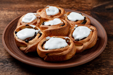 Buttery sweet buns with raisins on a brown clay plate. Covered with white sugar syrup.