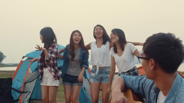 Group of Asia best friends teenagers give high five and dancing enjoy with guitar music happy moments together beside tents in national park. On the background beautiful nature, mountains and lake.
