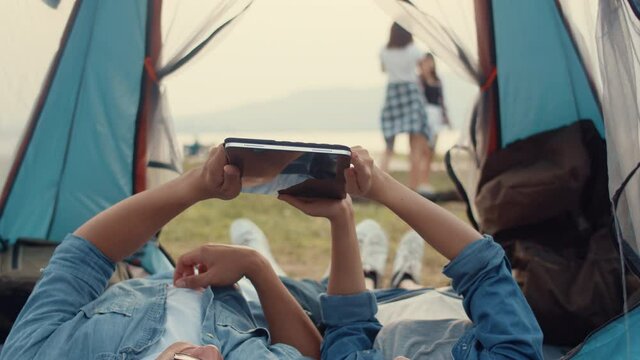 Couple Asia teenagers have relax time look photo album on tablet with happy moment togetherness in national park campsite. On background beautiful nature, mountains and lake. Travel blogger concept.