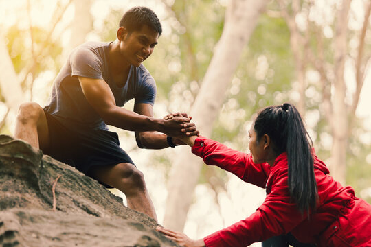A young man is helping to pull a woman hand to overcome obstacles.