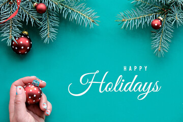 Christmas background, text Happy Holidays on turquoise textile. Top view on fir twigs decorated...