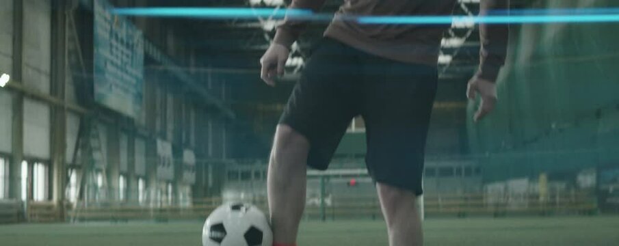 Anamorphic shot of athletic Caucasian man in sportswear juggling soccer ball with legs and head while practicing on indoor football field