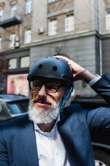 mature businessman in blazer adjusting helmet outside