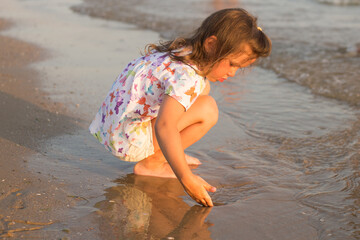 The little cute girl sitting and playing on the beach