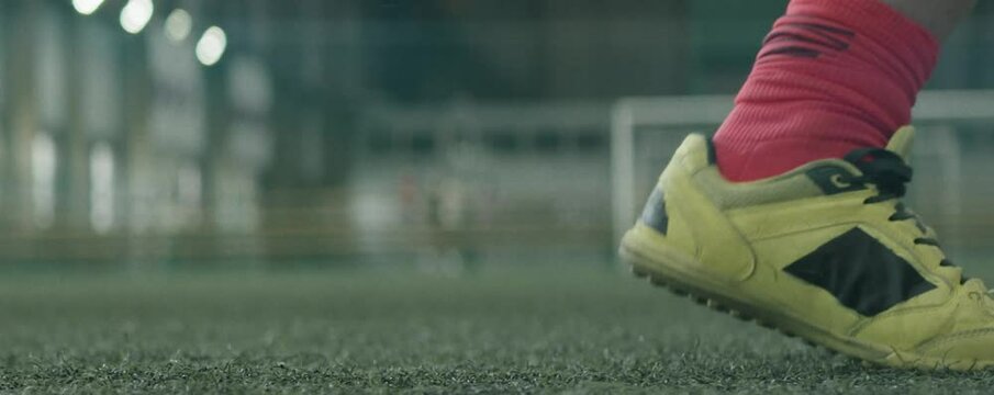 Close up anamorphic shot of feet of unrecognizable football athlete kicking soccer ball on indoor field