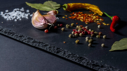 Spices on a stone plate. Black background. Black stone. Garlic, sea salt, pepper, chili, hot pepper, bay leaf