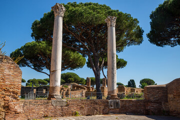 Obraz premium Rome Ostia Antica, Italy Ancient Roman ruins, columns with decorated capitals in Ostia Antica Rome Italy archaeological park, Roman port Tiber in summer with blue sky and pine trees. Italy.
