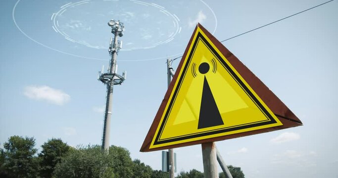 Animated EMF warning sign in front of a large cellular telecommunications tower antenna