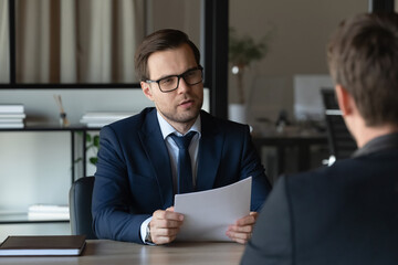 Serious concentrated employer with paper resume interviewing job candidate for hiring. Professional, lawyer, expert, advisor holding document, giving consultation to client. Business meeting concept