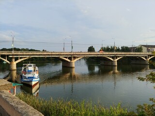 Fototapeta premium beautiful summer landscape with passenger boat docking on the river, concrete pedestrian bridge 