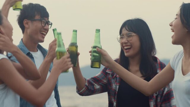 Group of Asia best friends teenagers dancing and drinking have fun salute toast of bottle beer enjoy party with happy moments together in campsite. On background beautiful nature, mountains and lake.