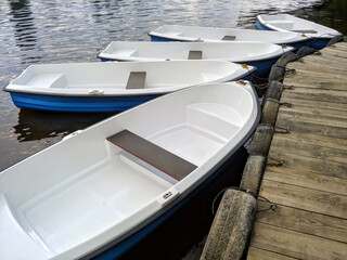 closeup photo of a few white plastic rowboats moored on wooden dock for fishing or boat trips on a river, lake