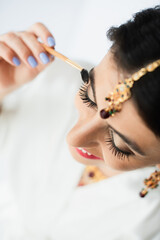 Obraz premium top view of happy indian bride with mehndi styling eyebrow with cosmetic brush on white