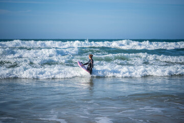 Girl with a surfboard overcomes the waves. Concept: Overcoming, Determination, Perseverance