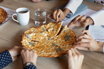Hot pizza on office table, hands of employees taking slices. Team of company workers ordering fast food delivery for lunch during meeting or party, eating takeaway unhealthy meal, junk food. Close up