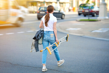 Woman crossing road and carrying medical crutches. Girl walks free after orthopedic injury and hold crutches in hand. Rehabilitation after bone fractures. Cure and recovery, healing medical concept