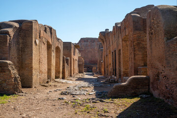 Rome Ostia site, ancient Roman ruins of a street with brick buildings from the imperial era in the Ostia Antica archaeological park in summer with blue sky. Rome Italy, Europe.