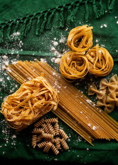 Mix of different varieties of pasta on green fabric background, cooking assorted macaroni concept