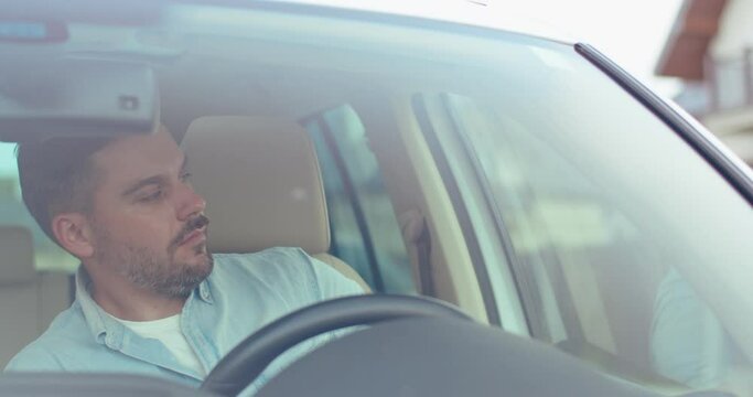 Young caucasian man opens the door and goes out of the car. Car's interior. View through the windscreen. Front view.