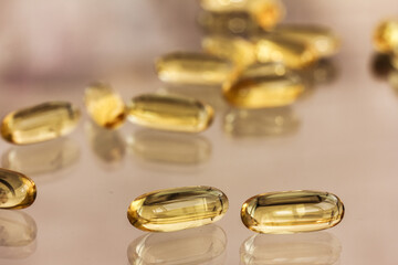 Two transparent yellow capsules close up and blurred capsules in the background. Omega, Omega 3, fish oil capsules and their reflections on glass background, table