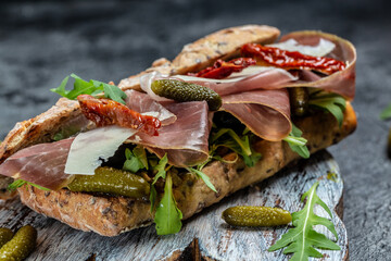 prosciutto sandwich, Ciabatta with prosciutto, sun-dried tomatoes, gherkins, parmesan and arugula, Food recipe background. Close up