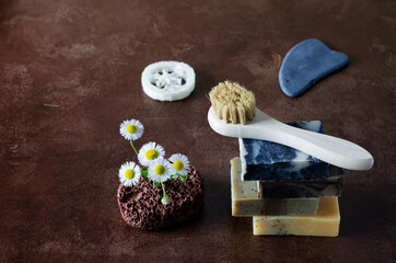 Cosmetic objects for body care, face - soap pieces, brush with natural bristles, stone, gouache on a brown background with copying space