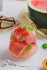 Glass of fresh watermelon cocktail with gin and soda, and garnished with mint leaves on light concrete background
