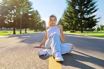 Fashionable trendy teenage hipster female sitting on road in park