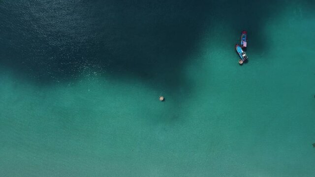 Aerial view of a remote coracle floating in the turquoise sea. Tropical paradise in southeast Asia. Picturesque seascape with colorful fishing boats.
