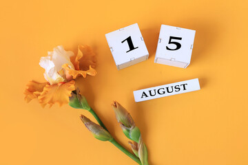 Calendar for August 15 : the name of the month of August in English, cubes with the number 15, yellow iris on a yellow background, top view