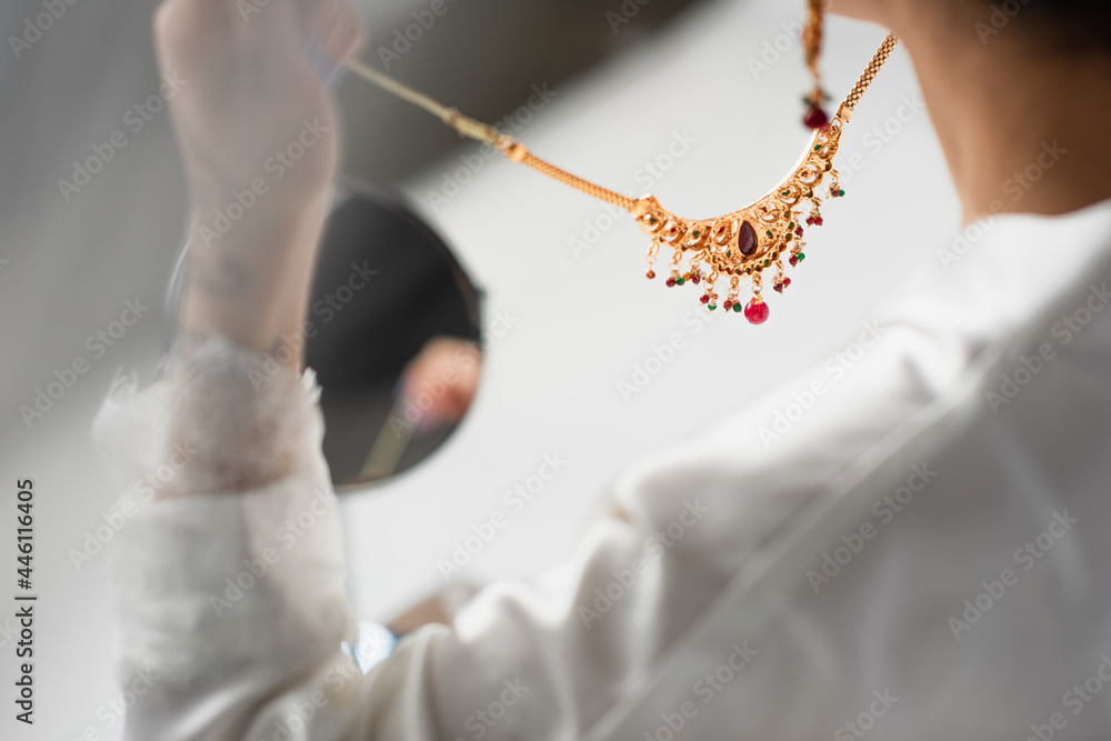 Wall mural cropped view of young bride holding necklace on white