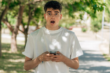 teenager boy with mobile phone and expression of surprise and amazement on the street