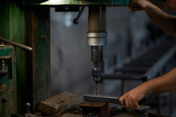 Close up of strong male hands using industrial drill press for making holes in metal construction. Craftsman processing steel at workshop. Manufacture concept.