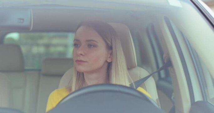 Confident young caucasian woman is driving a car on a road looking around. Feel happy, listening to music. Good mood. Enjoy. Car's interior. Front view. Close up.