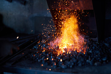 Red hot metal in burning fire preparing for forging process at workshop. Sparks flying around....