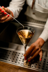 glass with drink on bar counter and hand of bartender with pipette above it