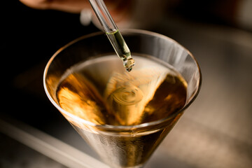 close-up of tip of pipette from which drop of liquid falls into glass