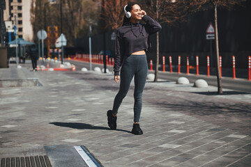 Obraz premium Smiling pleased sportswoman in wireless headphones talking on the smartphone