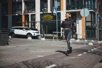 Cheerful slim woman in wireless headphones jogging ahead