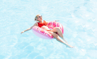 Woman relaxing on donut lilo in the pool at private villa. Inflatable ring and mattress. Summer holiday idyllic. High view from above - obrazy, fototapety, plakaty