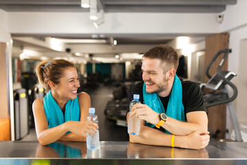 happy couple with towels ismiling and holding water bottles while resting in a fitness club