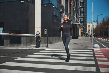 Fototapeta na wymiar Smiling joyful young female runner jogging ahead