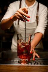 close-up of female bartender gently stirring with spoon cocktail in transparent mixing cup