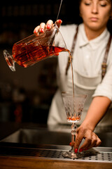 female bartender gently pours drink from glassy mixing cup with strainer into glass