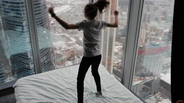 Cute teenage girl jumping on the bed near the window city view from above