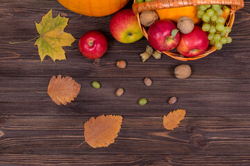 Orange pumpkins with apples and pears in a basket with grapes, nuts and leaves on a brown wooden table. View from above. Harvest concept.