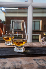 Dram of single malt scotch whisky served in tasting glass with view on old window and houses