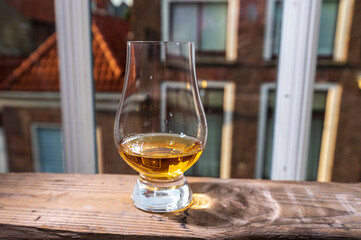 Dram of single malt scotch whisky served in tasting glass with view on old window and houses