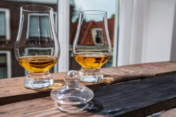 Dram of single malt scotch whisky served in tasting glass with view on old window and houses